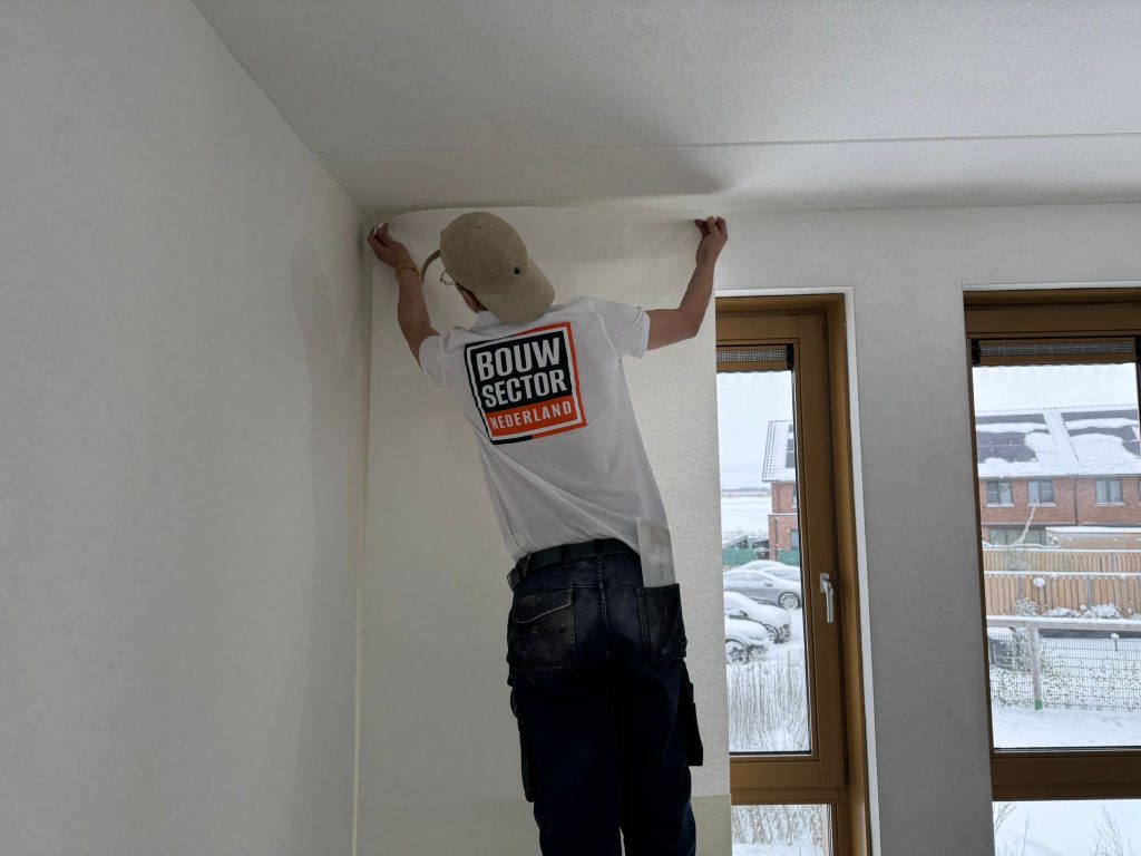 Behanger van Bouwsector Nederland zet een baan renovlies bovenaan strak tegen het plafond