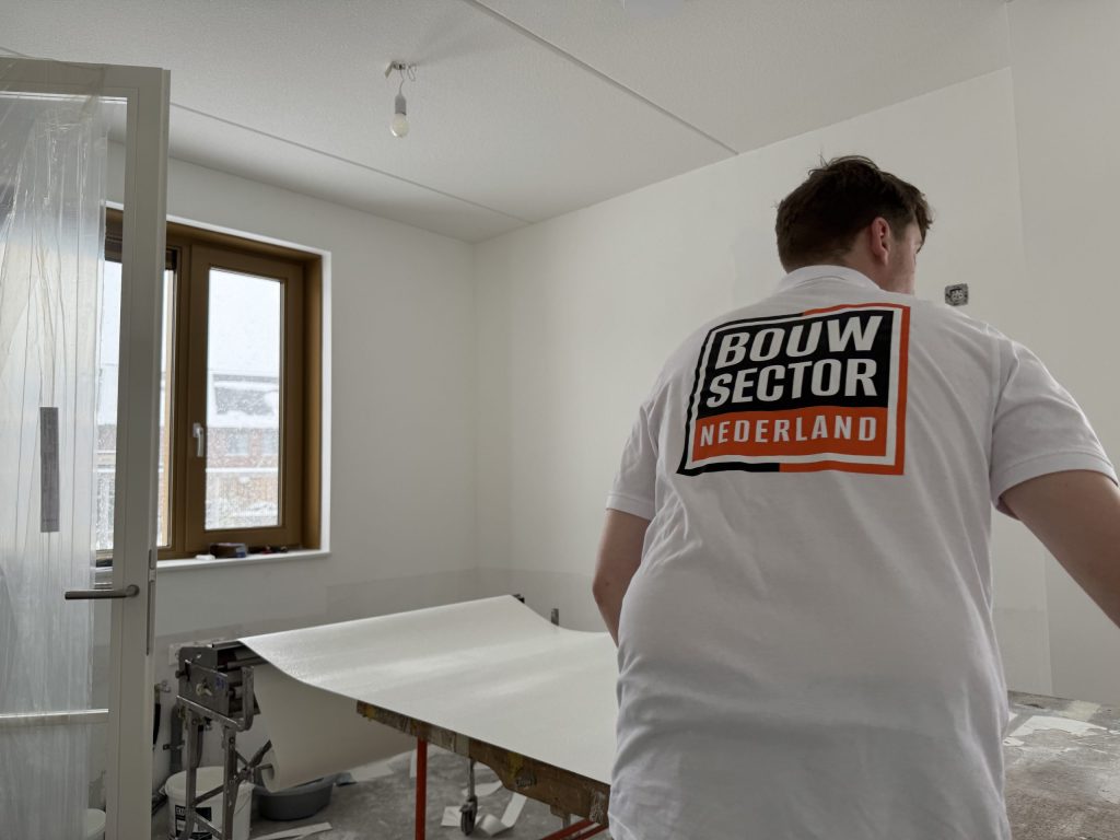 Behanger in een wit shirt van Bouwsector Nederland rolt een baan renovlies uit over de plaktafel