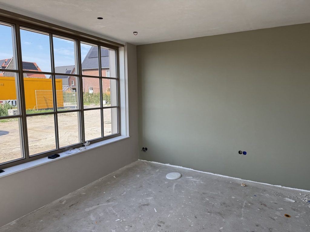 Nieuwbouwkamer met een groot raam en een wand die al grijsgroen is gesausd