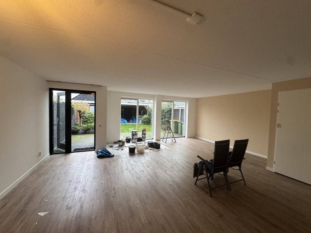 Lange woonkamer met tuindeuren, laminaat en verfemmers bij het raam